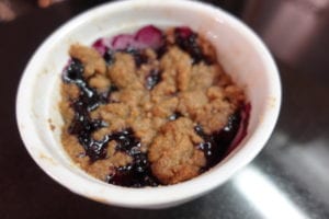 Bubbling hot blueberry crumble for one showing crispy topping similar to cobbler and fruit filling just peaking through